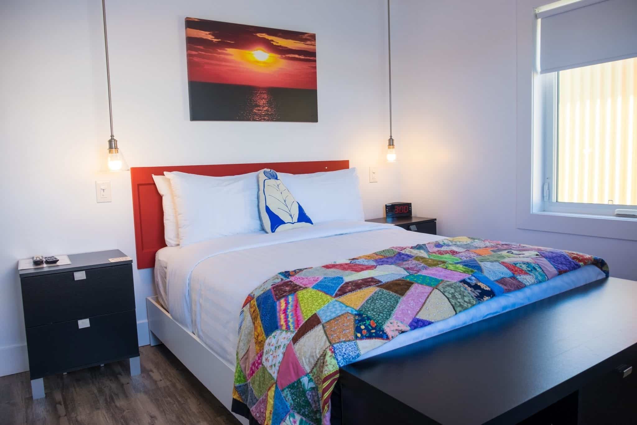 A white bed in a white room with a brightly colored patchwork quilt at the foot of the bed in Twillingate, Newfoundland.