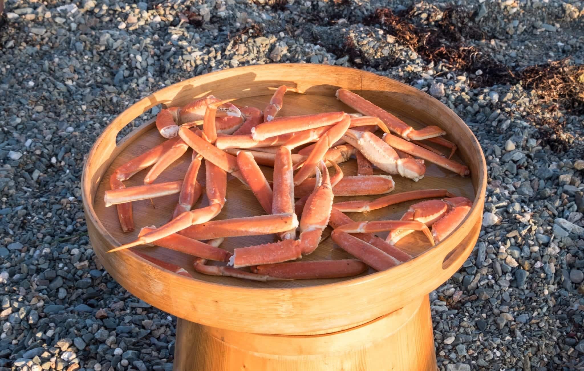 Crab legs, cooked and on a wooden serving platter on the beach.