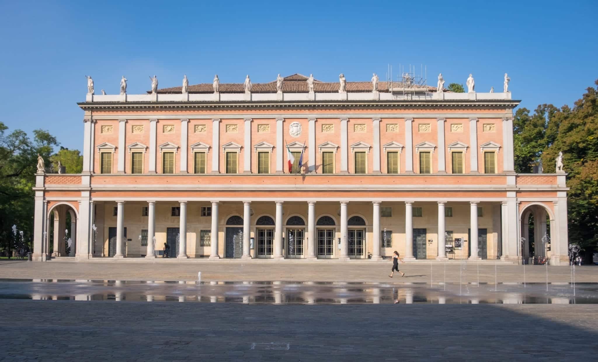 A bright orange building with lots of columns underneath a blue sky.