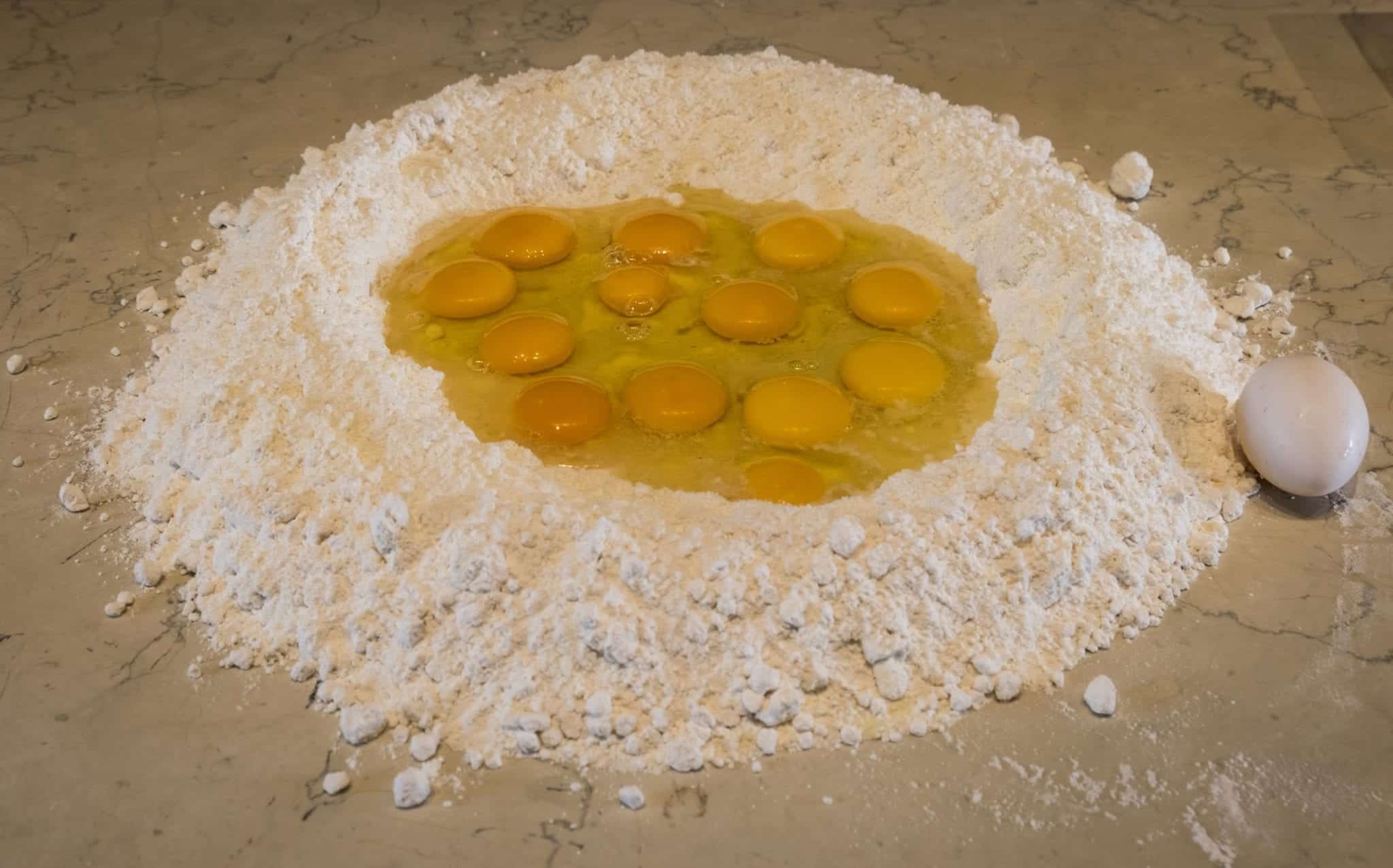 A giant mound of flour with twelve raw eggs sitting inside it.