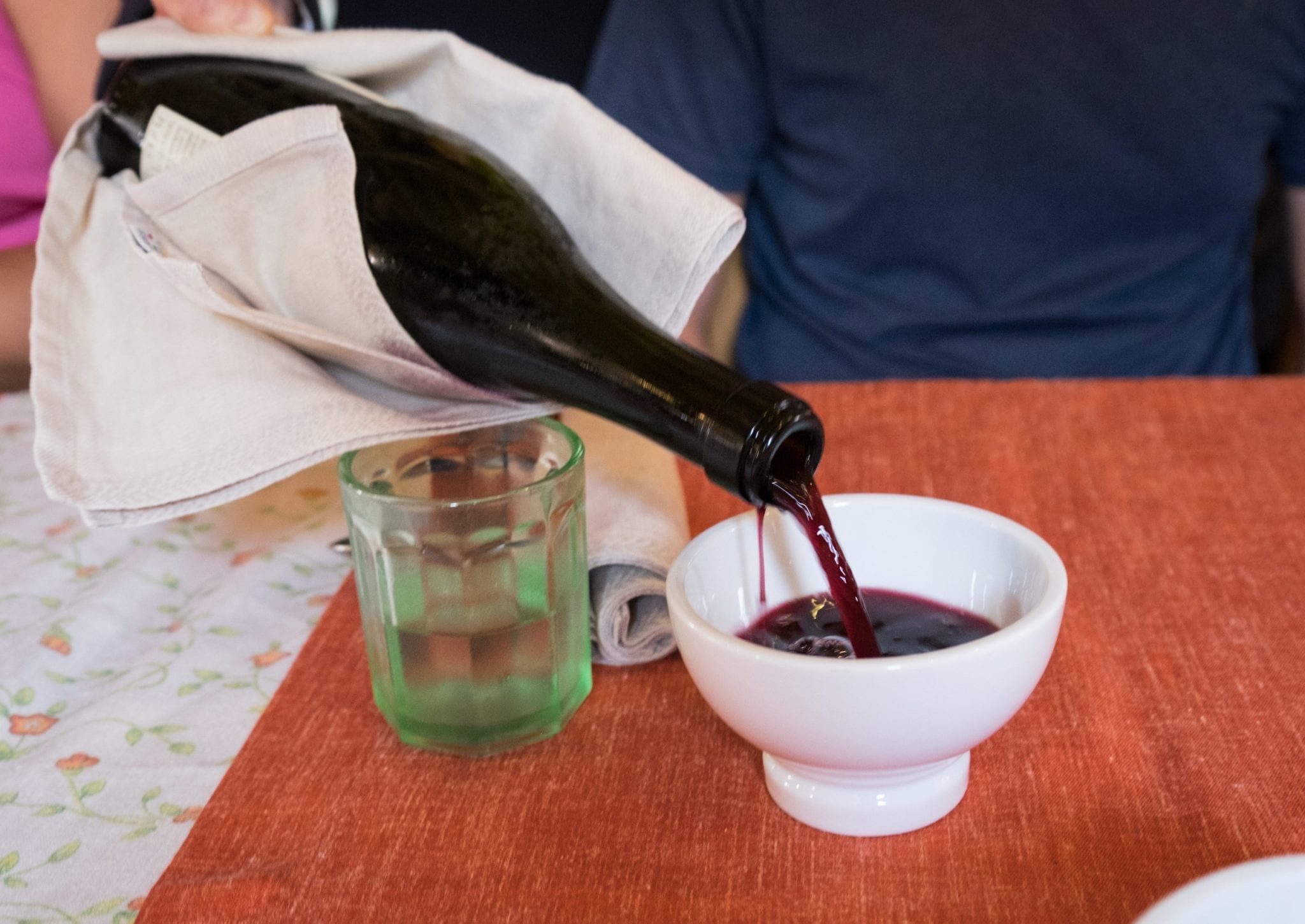 A bottle of red wine being poured into a small white bowl for drinking.