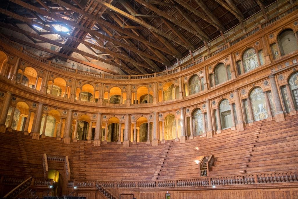 An old-fashioned giant theater with wooden benches in stadium-like seating, with wooden arches on top.