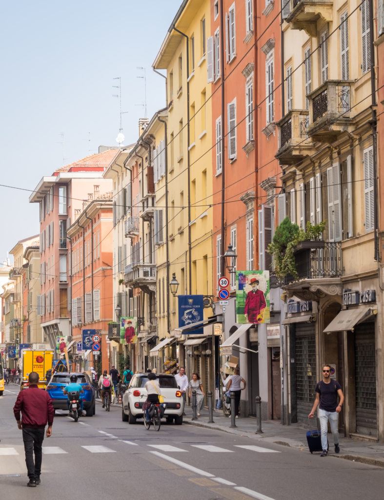 People walking down the streets surrounded by warm-colored buildings in Parma, Italy.
