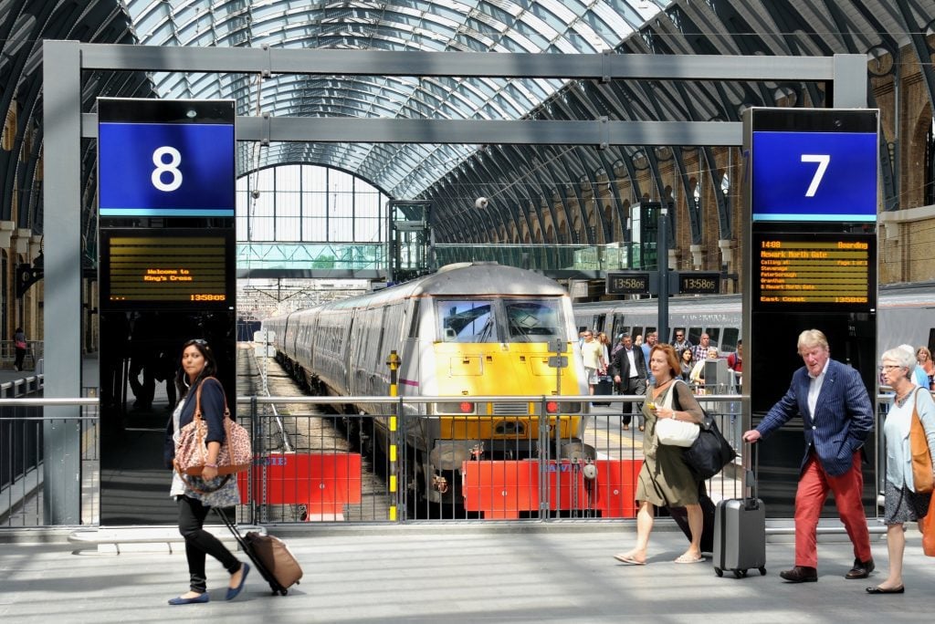 A bright yellow train in London's King's Cross station and people walking by with suitcases.