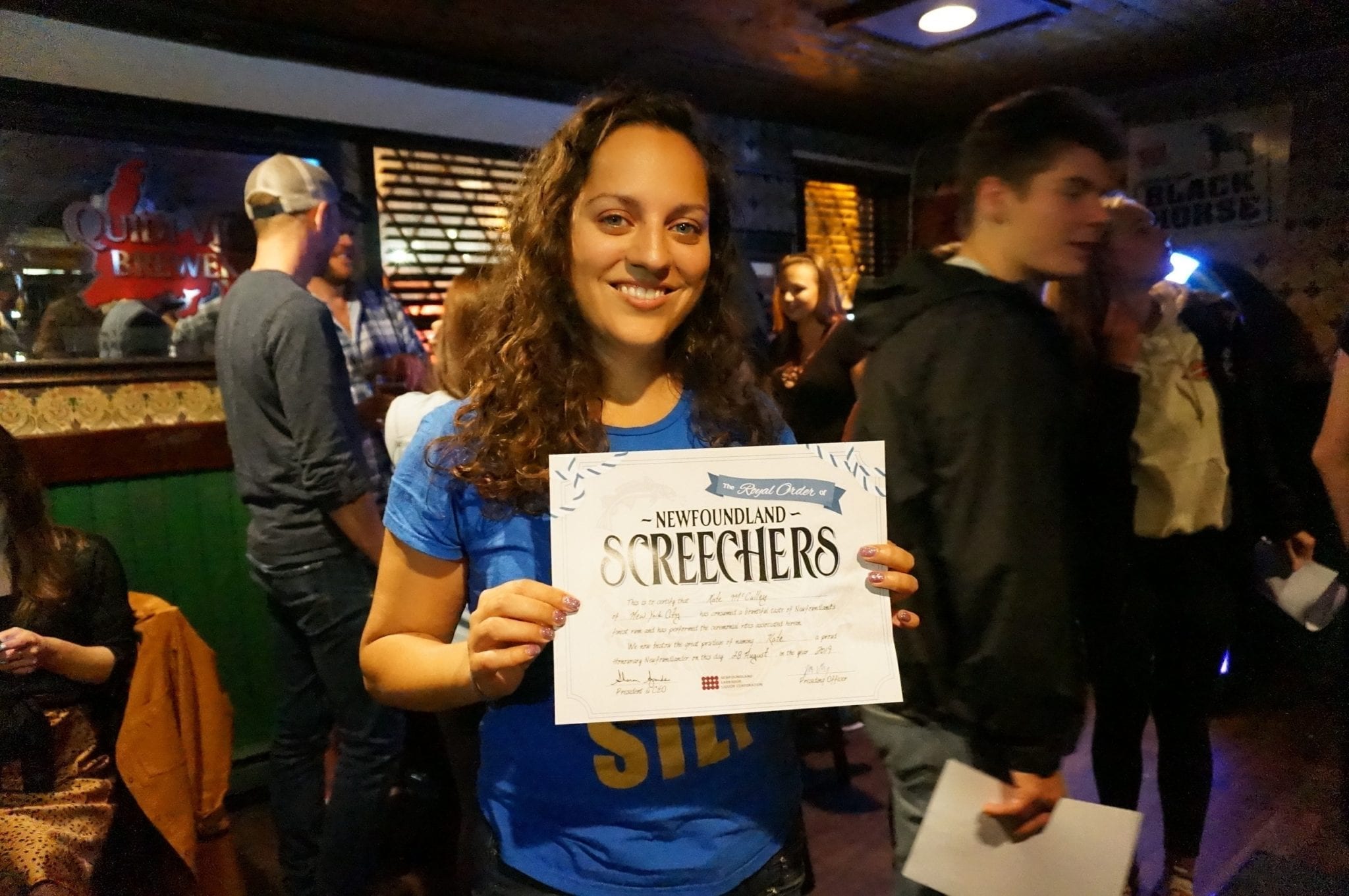 Kate stands in a bar holding a certificate that says "SCREECHERS".