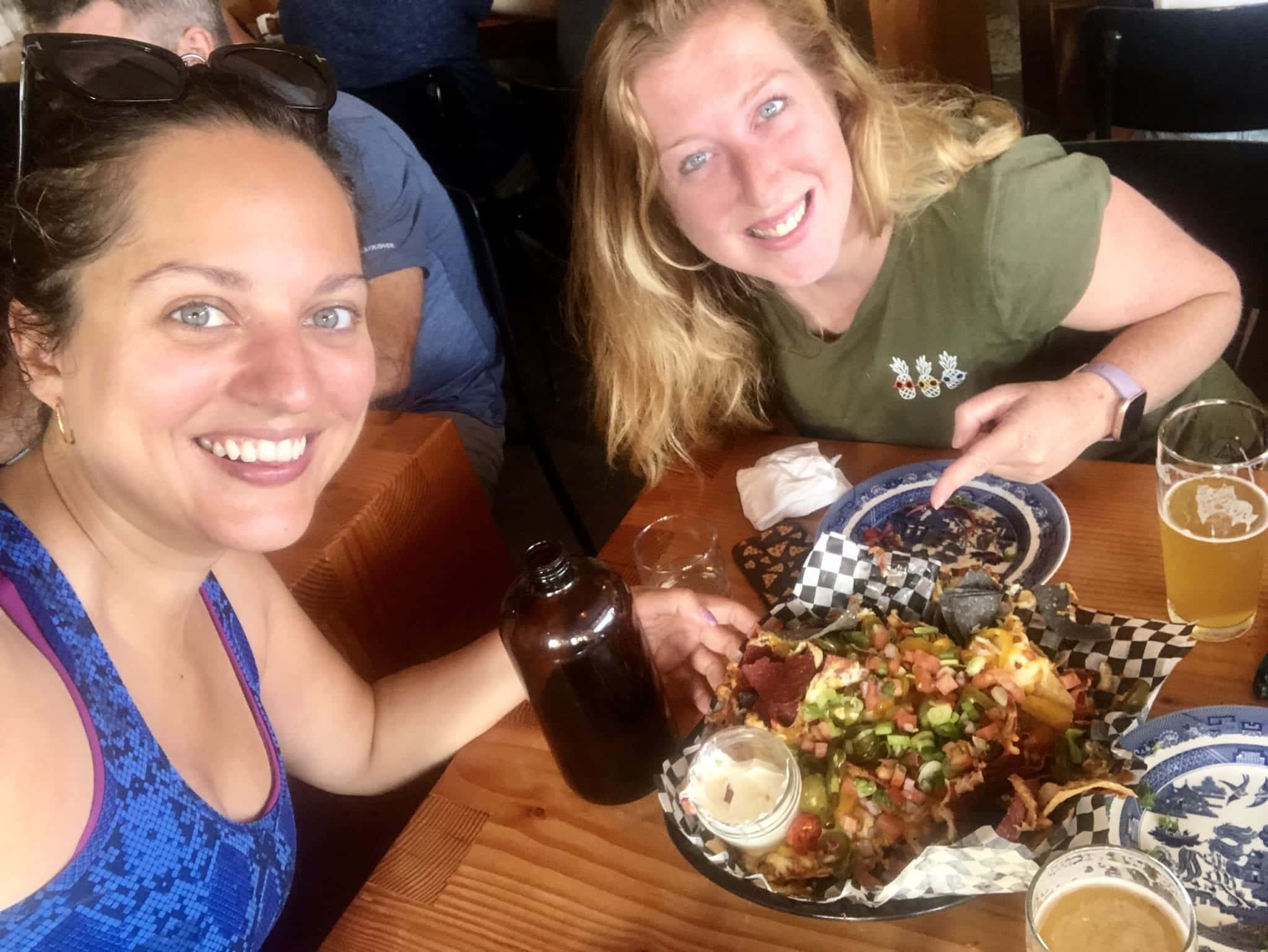 Kate and Candice pose for a selfie with beers and nachos.