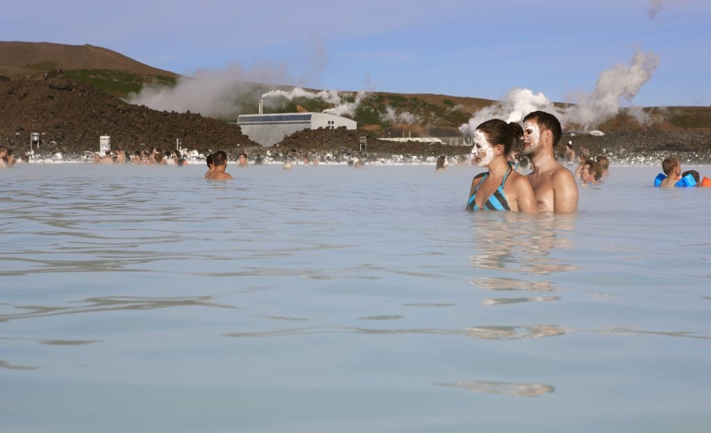 A man and a woman wearing silica mud masks while relaxing in the Blue Lagoon.