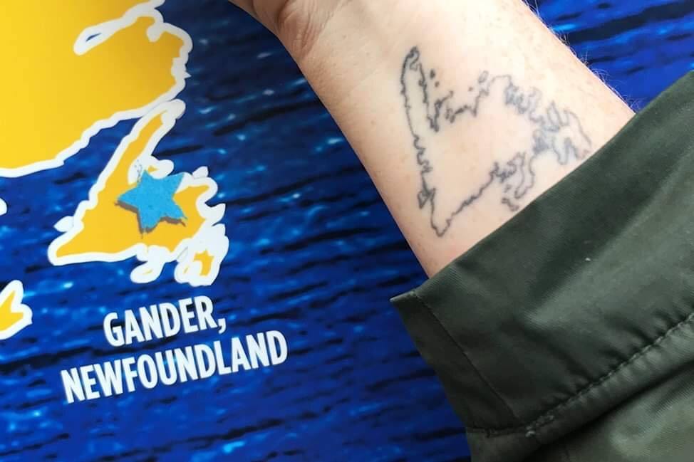 Candice's tattoo of Newfoundland on her wrist, next to a promotional sign for the musical Come From Away.