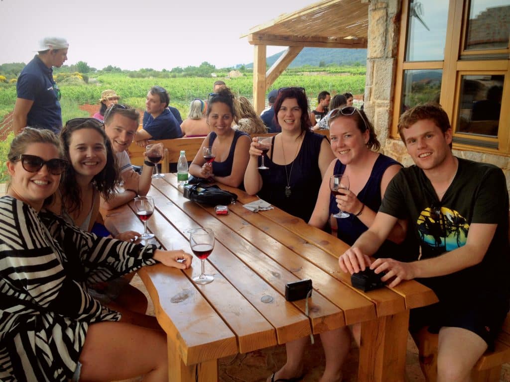 A group of friends sitting around a wooden table sharing some wine.