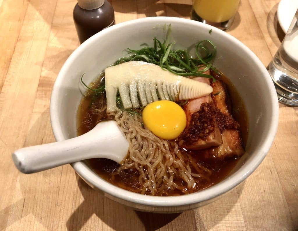 A bowl of ramen with noodles, pork belly, bamboo, and an egg yolk at Momofuku Noodle Bar.