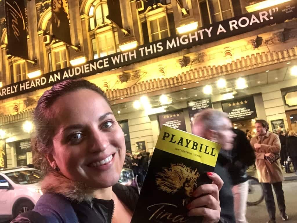 Kate holds a "Tina" playbill in front of the theater