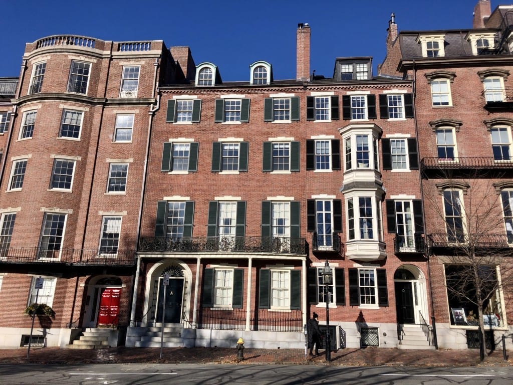 A row of fancy Beacon Hill brownstones in Boston beneath a bright blue sky.