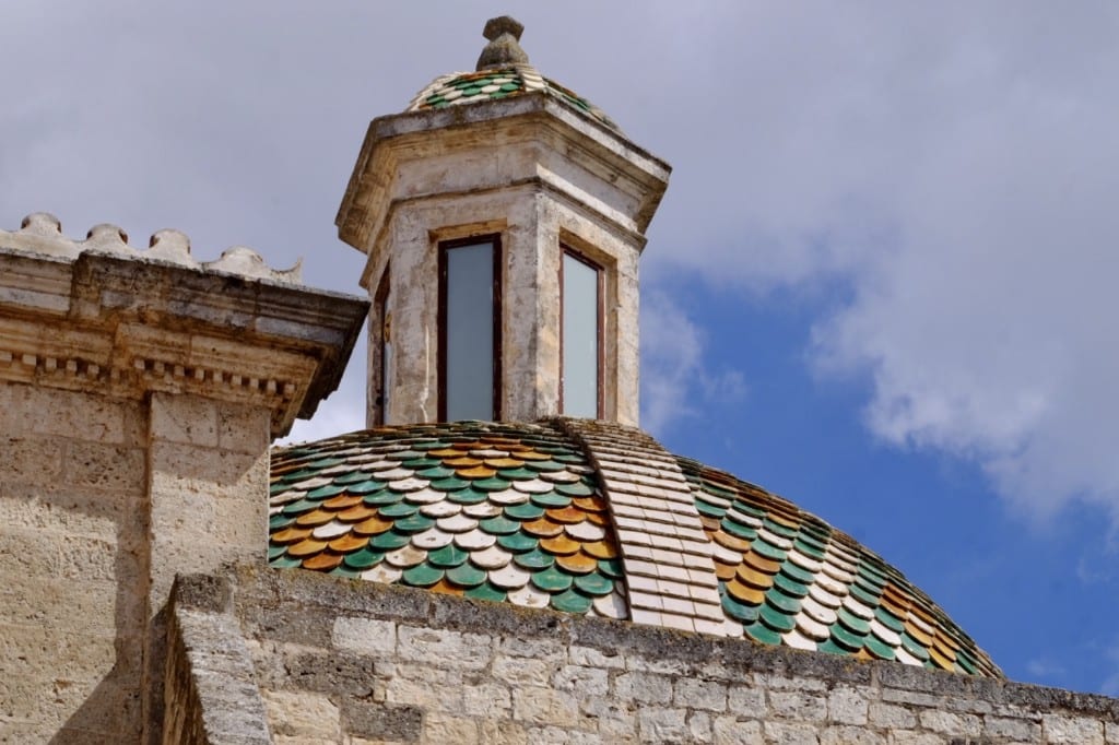A church dome topped with green, orange, and white tiles in Ostuni, Italy.