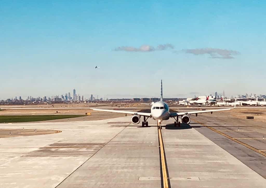 A plane cruises the runway at JFK, the New York skyline far in the background.