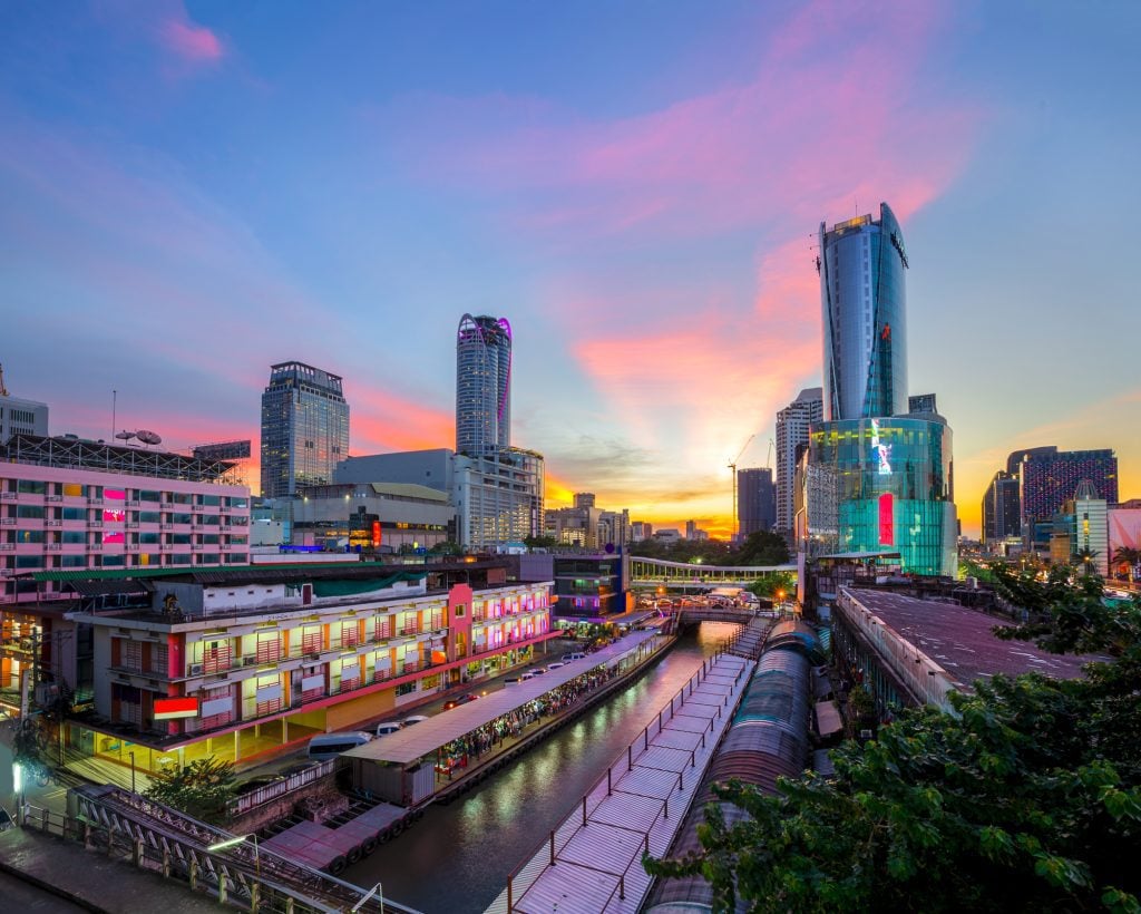 A wooden pier on a narrow canal in Bangkok, with skyscrapers in the background.