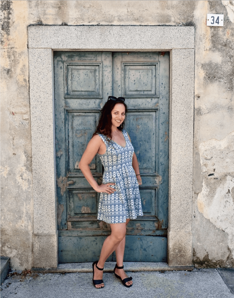 Kate wears a green dress and stands in front of a green door in Lake Orta.