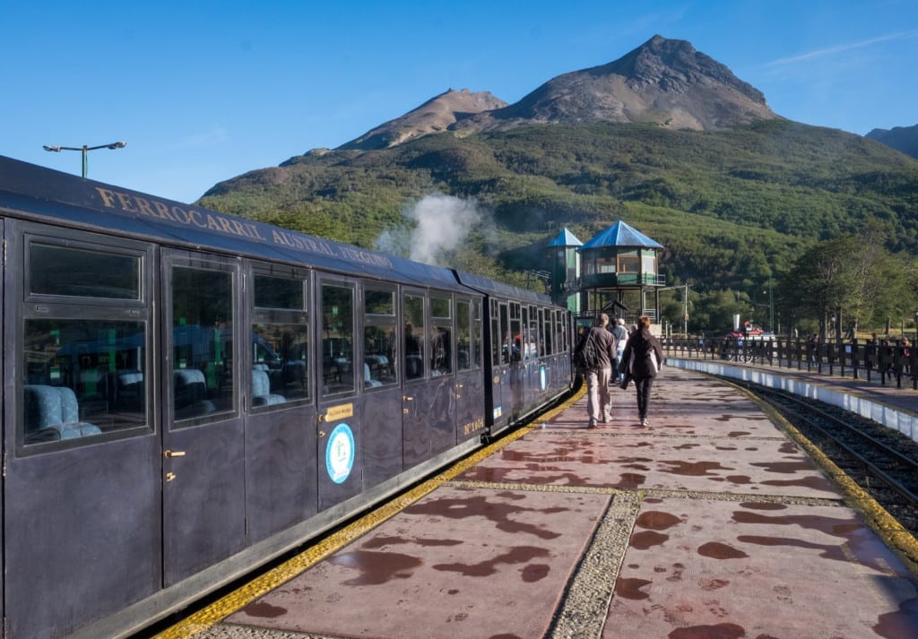 A silver passenger train picks up passengers in the mountains.