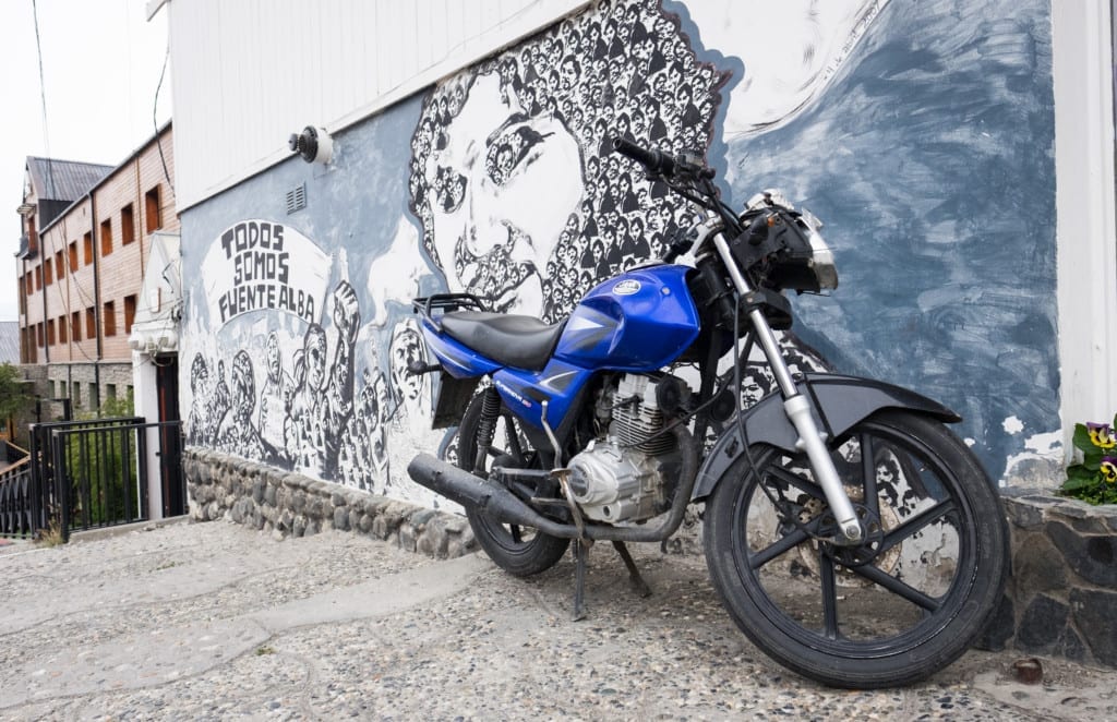 A blue motorbike in front of black and white street art in Ushuaia.