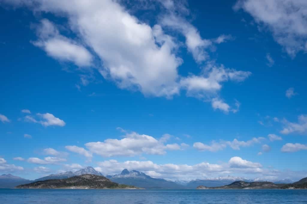 Mountains along the Beagle Channel, a bright blue sky with fluffy clouds overhead.