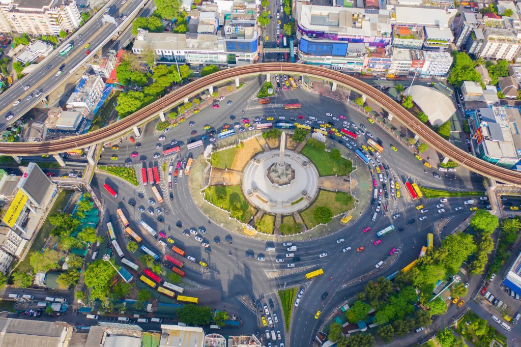 Aerial view of Bangkok's Victory Monument, with a rotary of cars driving around a small park with a tall obelisk on it.