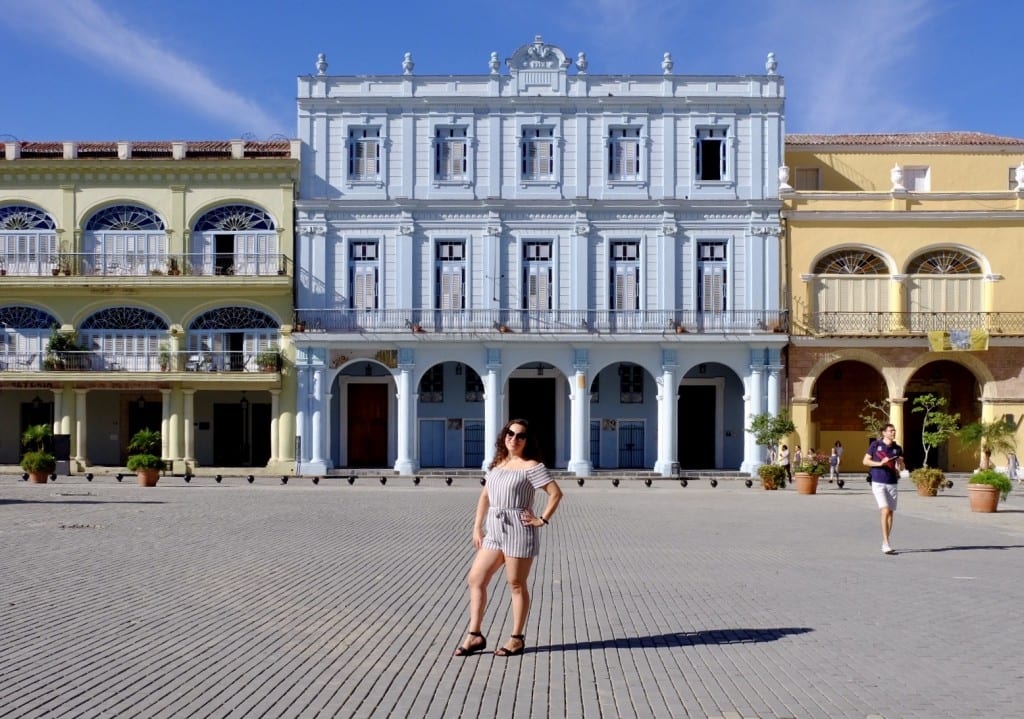 Kate stands on a plaza in front of blue and yellow colonial buildings in Havana.