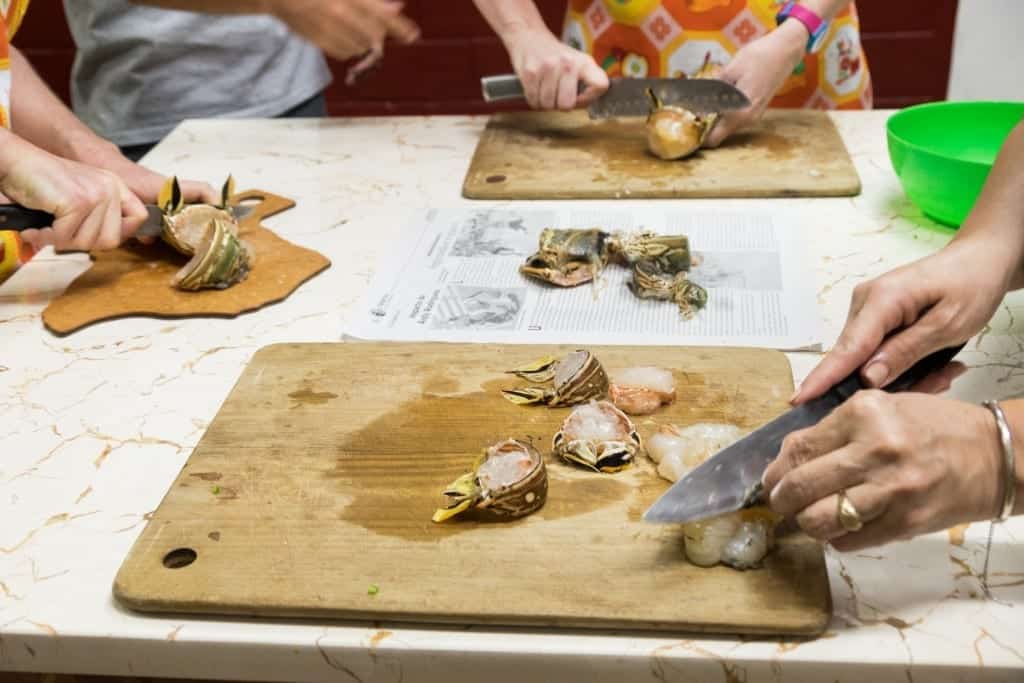 Three sets of hands chopping the raw lobster, still in its shell.