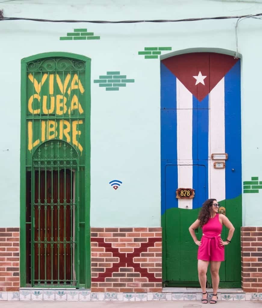 Kate stands in front of a mural in Cuba reading "Viva Cuba Libre" with a Cuban flag.