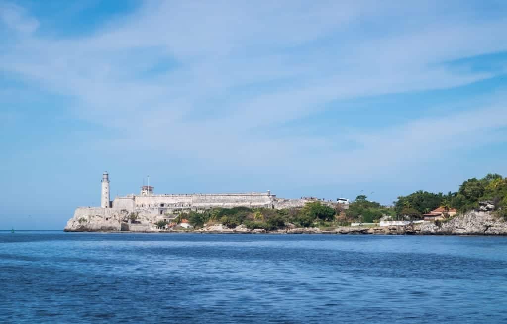 A view of the lighthouse on the ocean in Havana underneath a blue sky.