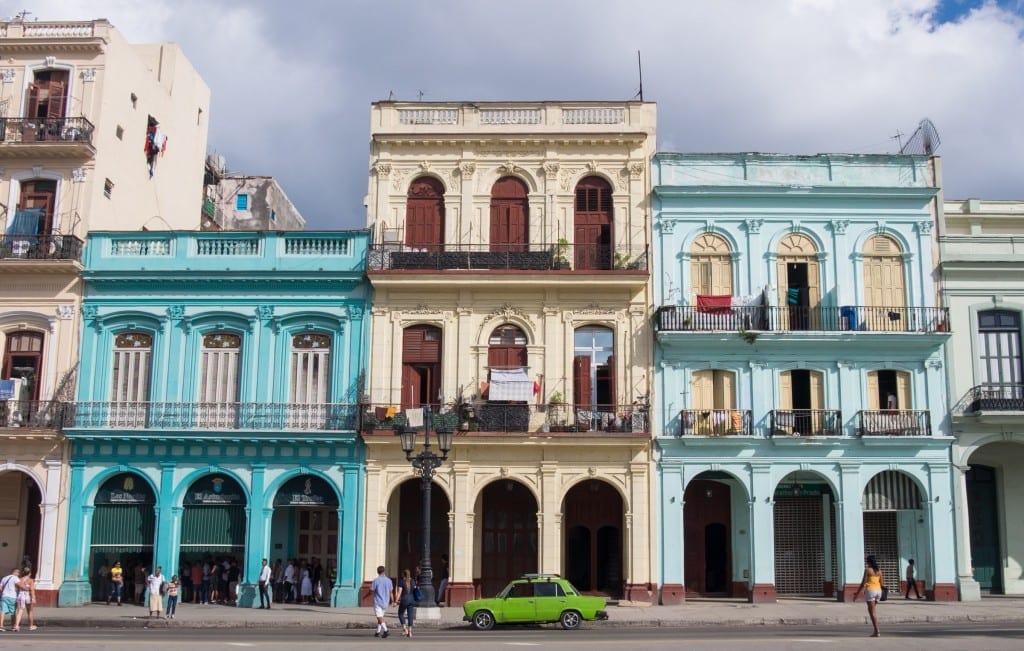 A bright green car in front of blue and white colonial homes in Havana.