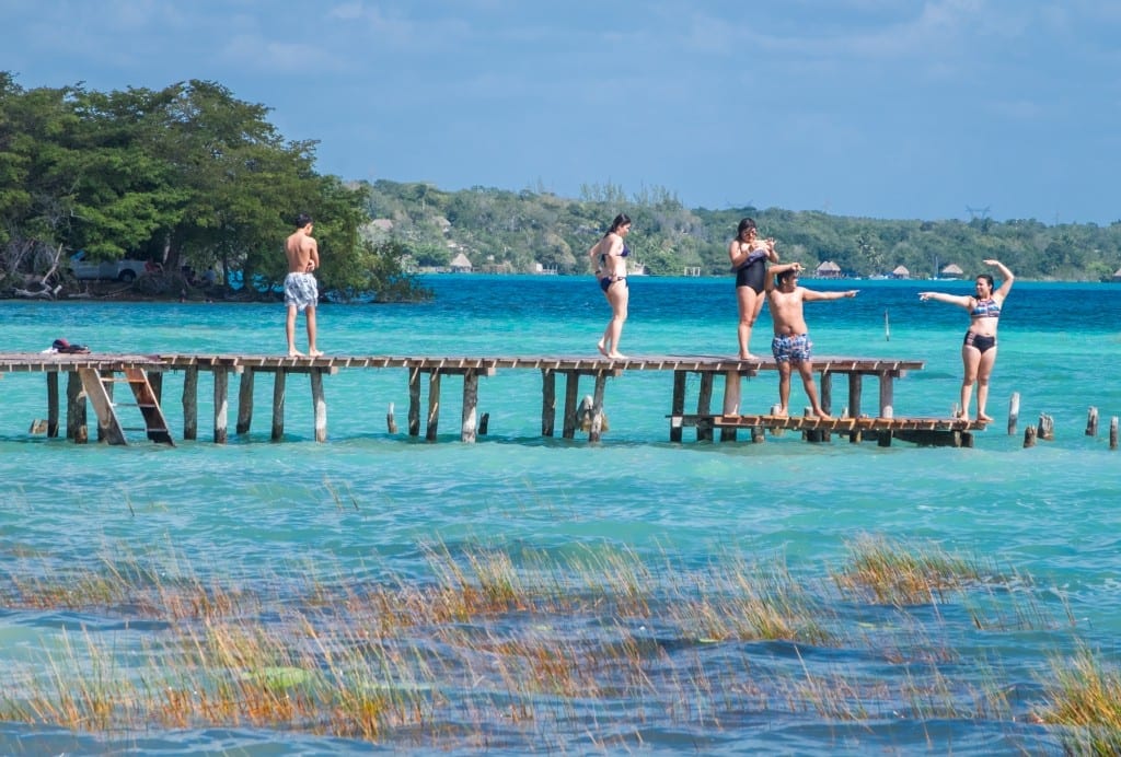 A group of friends having fun and posing on a dock on top of bright neon water in Bacalar.