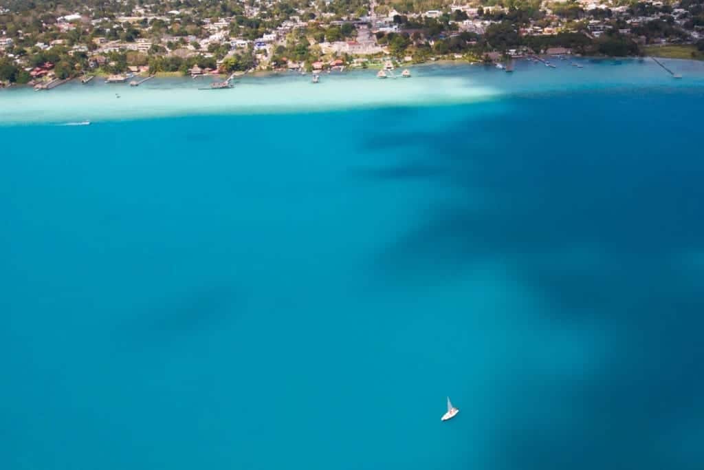 An aerial view of the bright blue lake, a tiny sailboat in the abyss.