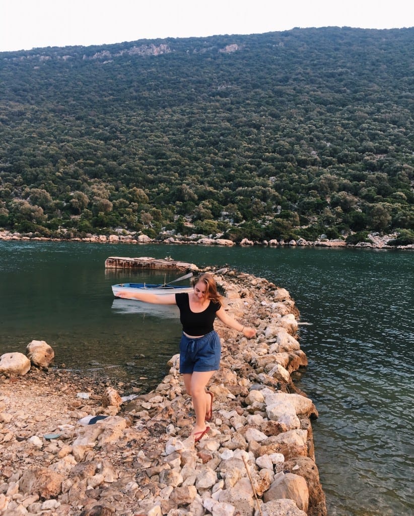 Katie balancing on a rocky jetty in the dark green Mediterranean.