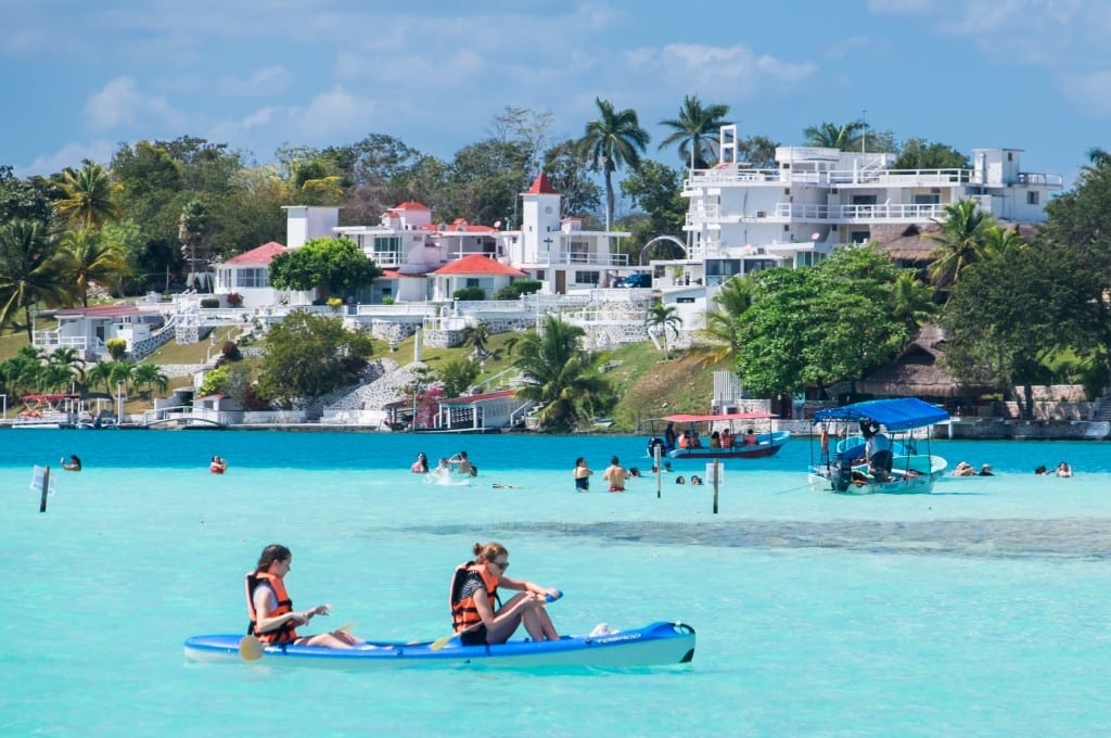 A group of people swimming and kayaking in very pale blue water.