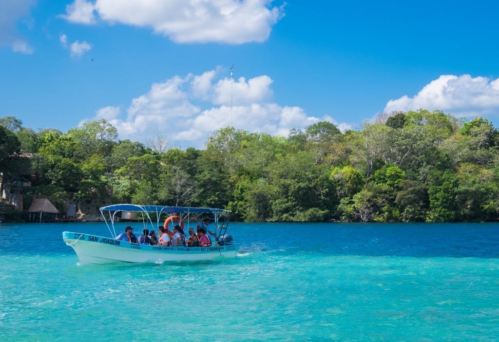 A boat full of people perched in a lake right on a line where one side is bright turquoise and one side is dark blue.