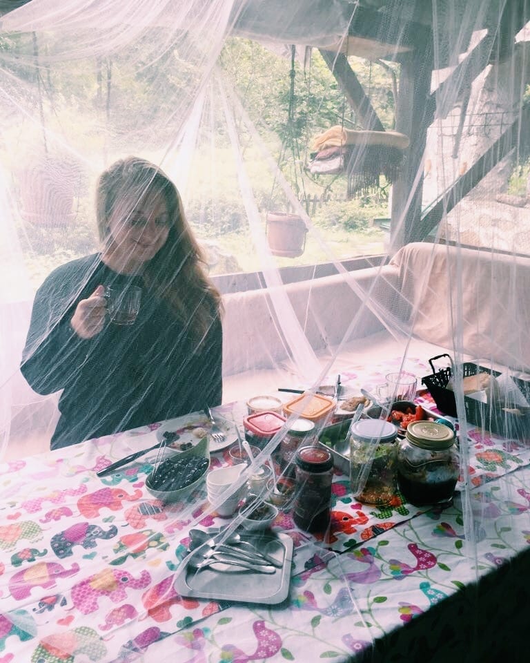 Katie sitting down to a meal underneath mosquito netting, smiling and drinking a cup of tea.