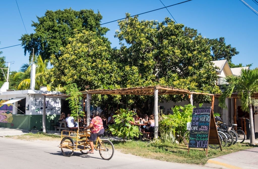 A woman riding a bike past an outdoor restaurant.