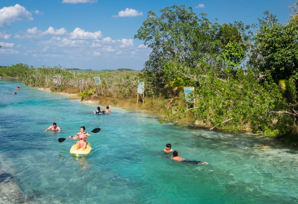 A group of people swimming and kayaking in a bright turquoise river.