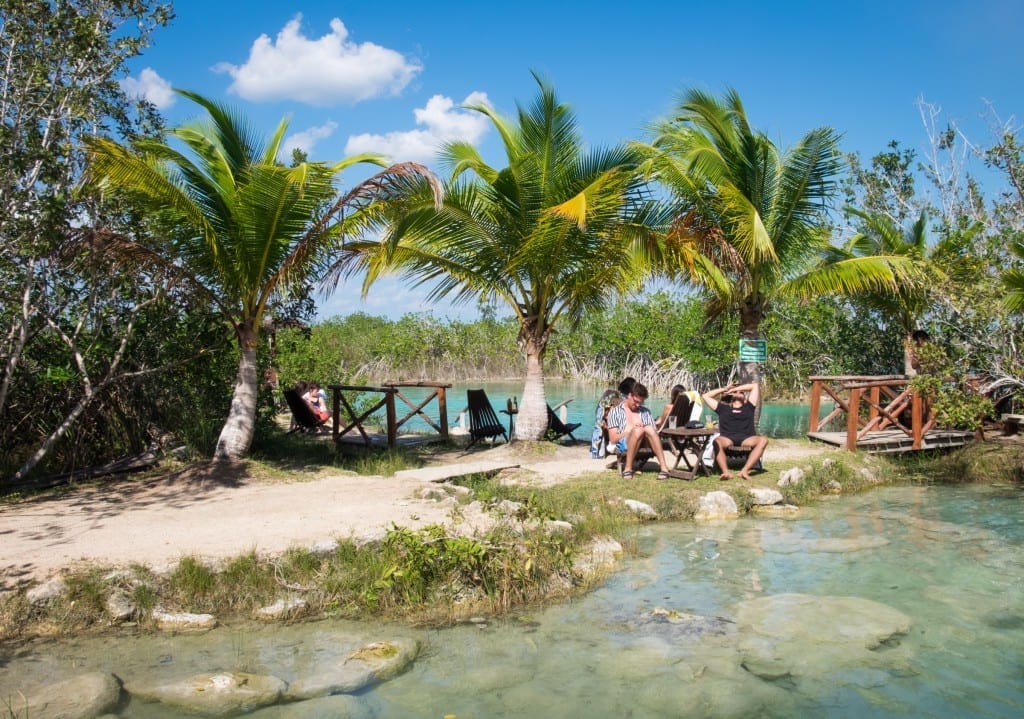 People relax on the shore of a lake, drinking cocktails and enjoying the sun.