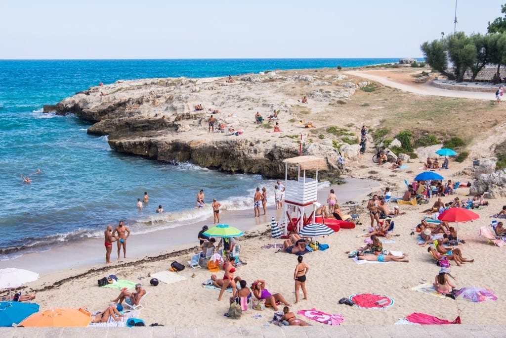 People relaxing on the jagged rocky beach of Monopoli, Italy.