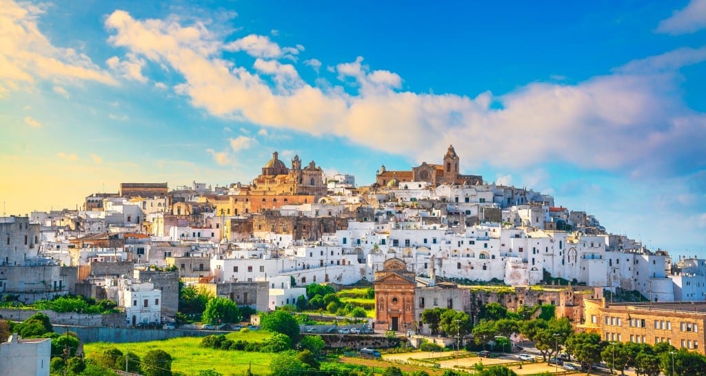 A bright white city in Italy perched on a hill underneath a bright blue sky.