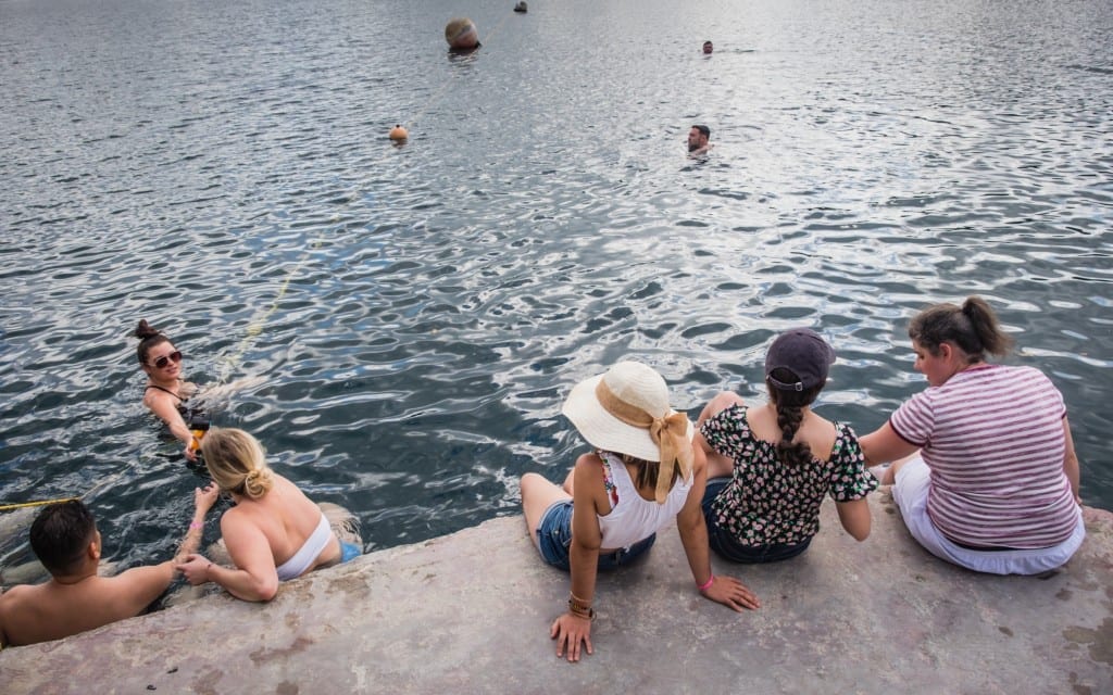 A group of girls on shore dipping their feet into the water as people swim.