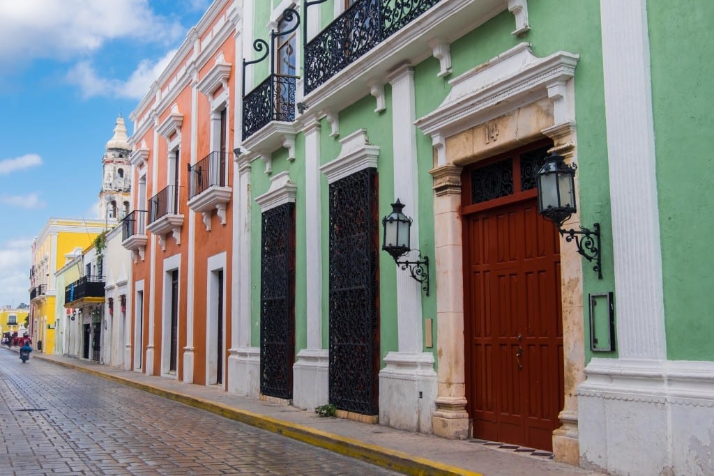 A bright stately street with orange and green buildings with white trim in Campeche, Mexico.