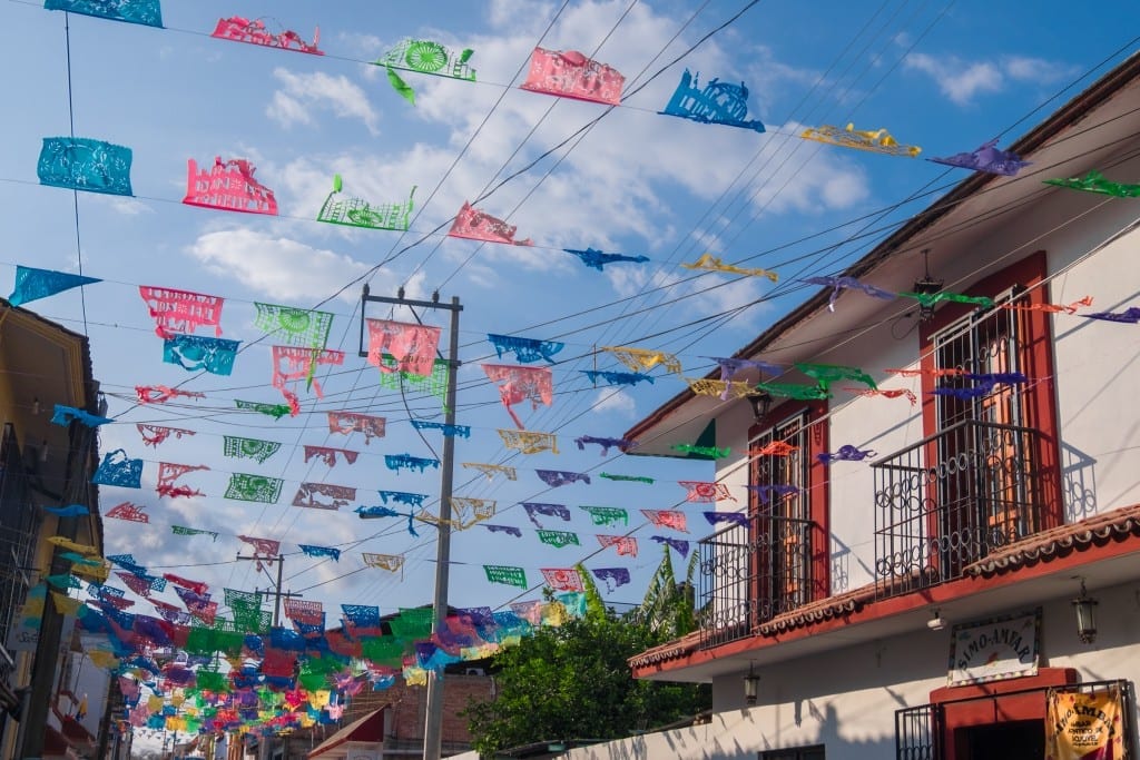 Colorful paper flags hanging on lines between Mexican buildings.