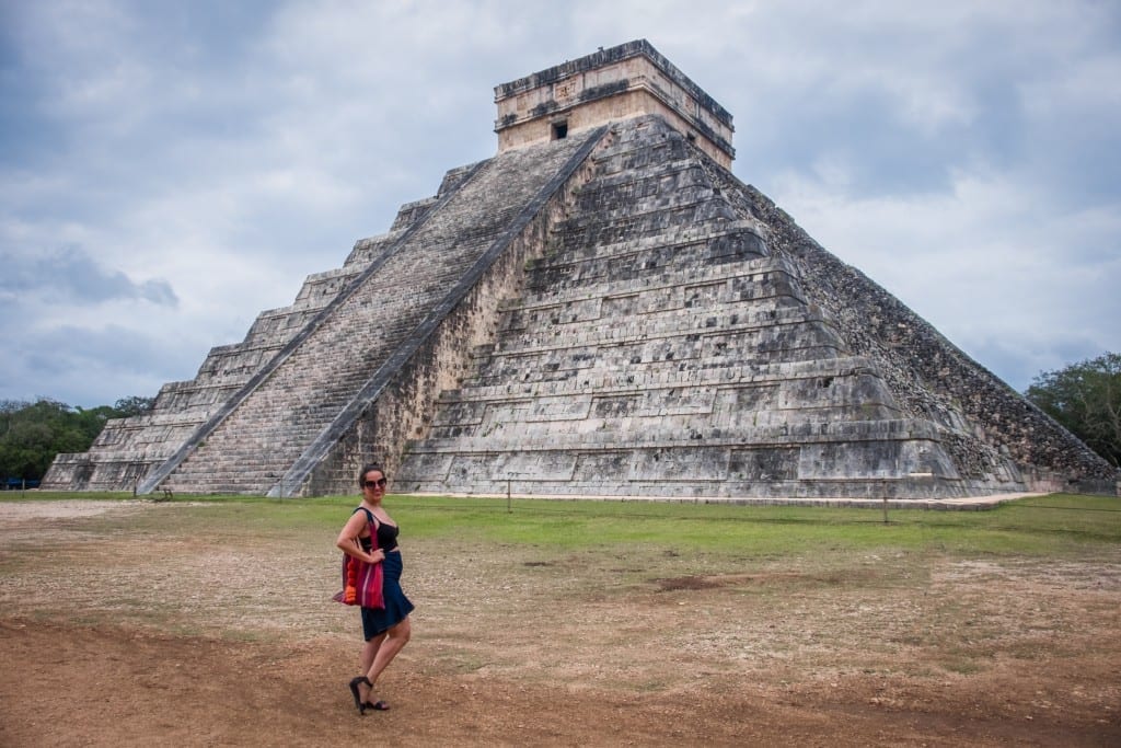 Kate standing in front of the gray stone pyramid of Chichen Itza in Mexico. The sky is cloudy and Kate miraculously has no other people in the photo.