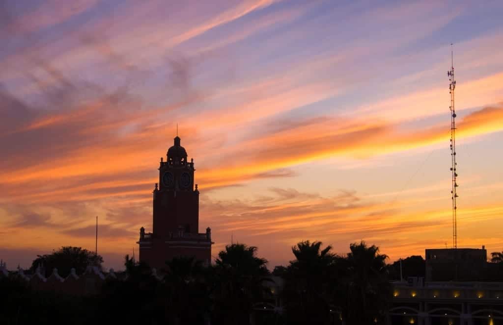 The outline of a church tower silhouetted by a pink and orange sunset.