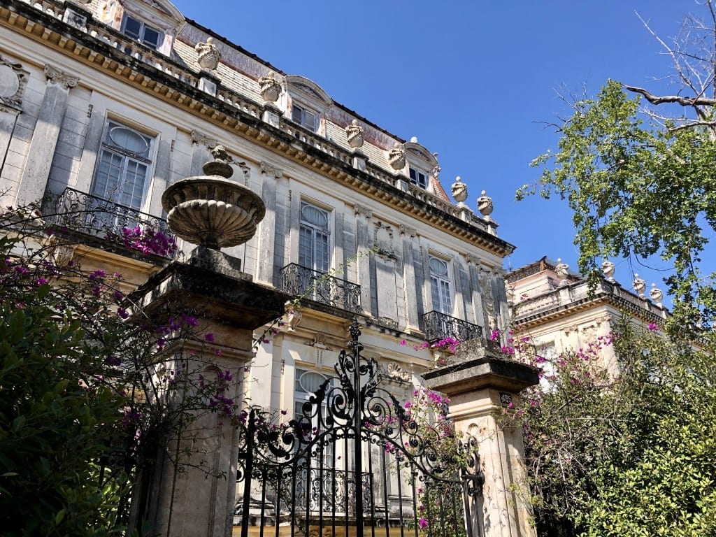 A wrought-iron gate in front of a stately mansion.