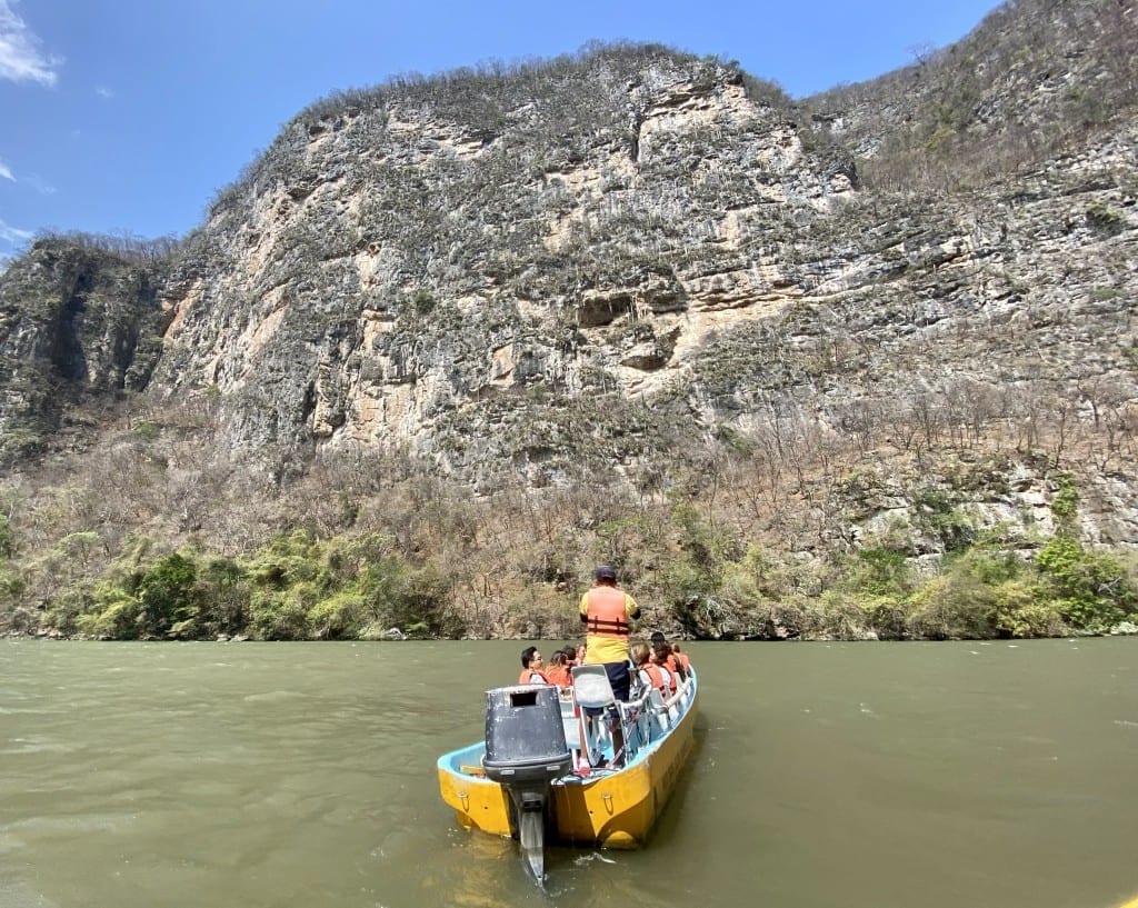 A bright yellow speedboat driving up toward a canyon wall.