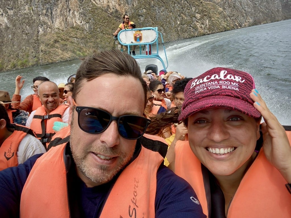 Kate and Charlie taking a smiling selfie in the front of the speedboat, clearly going fast, their hair blown back.