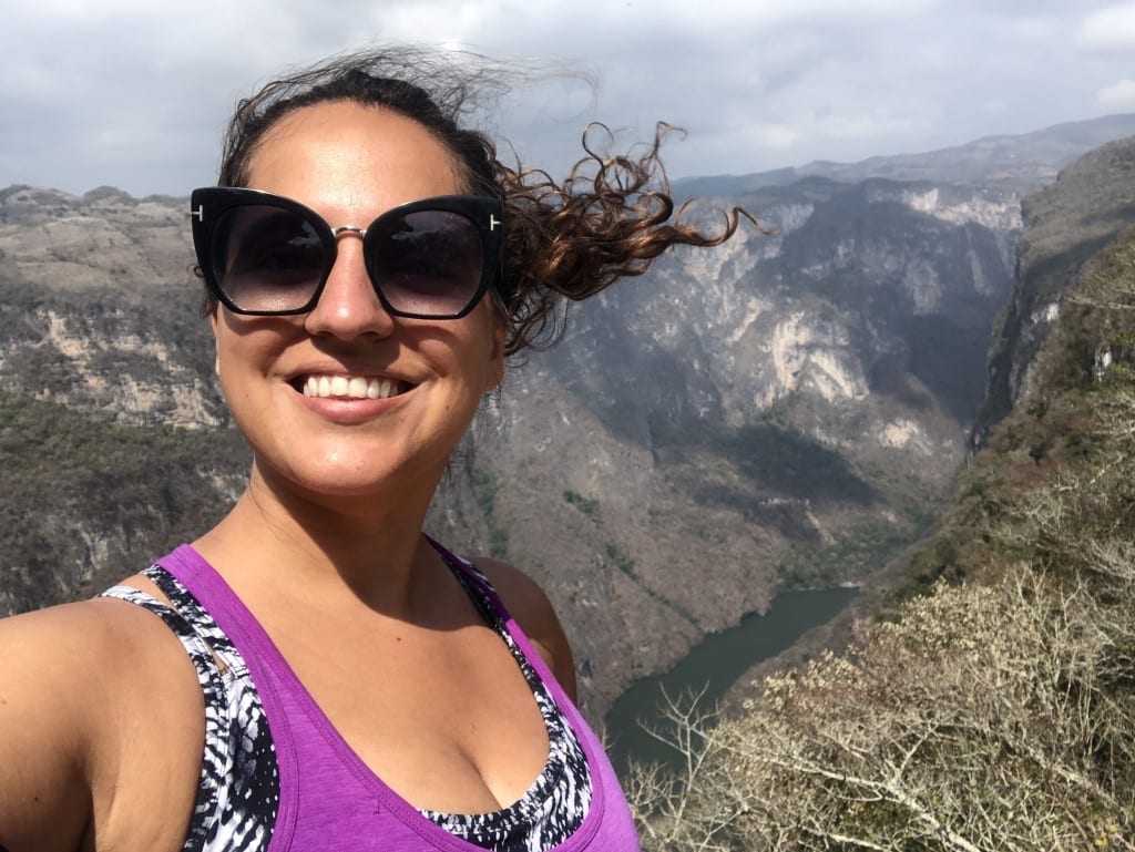 Kate takes a selfie wearing sunglasses, the canyon below her.