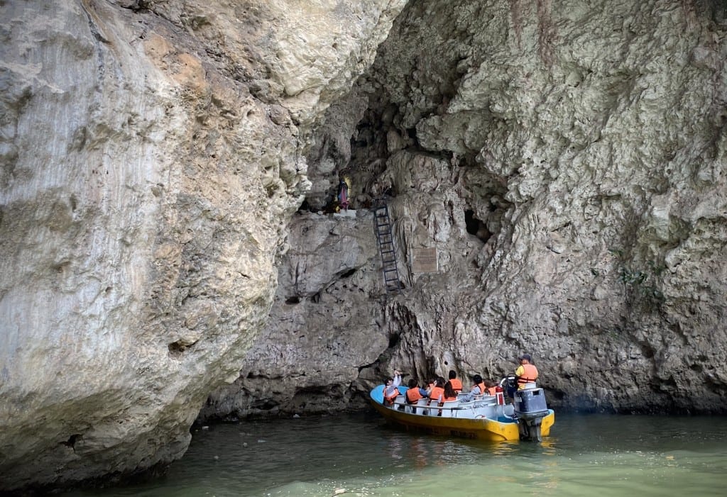 A speedboat entering a cave with a ladder leading to a Virgin Mary statue.